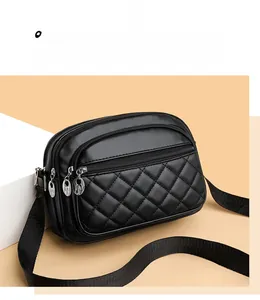 Detail of black quilted crossbody bag with three zipper compartments on modern props