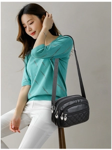 Quilted black crossbody bag with multiple zippers shown on a mint green knit top