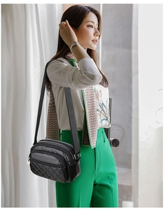 Detail of black quilted crossbody bag with adjustable wide strap and metallic pendant