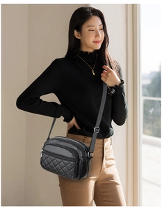 Detail of a black quilted crossbody bag with adjustable strap worn by a model in casual attire