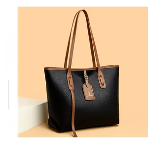 Dettaglio borsa tote in pelle nera con sottili manici marroni e targhetta del marchio