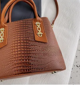 Detail of brown crocodile embossed tote bag with gold chain hardware and metal feet