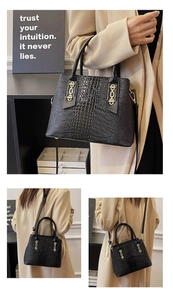 Detail of black crocodile-embossed tote bag with gold rings and adjustable shoulder strap