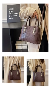 Detail of brown crocodile embossed handbag featuring gold H-buckle and tubular handles