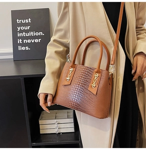 Close-up of caramel brown crocodile embossed handbag with gold chain detail on beige coat