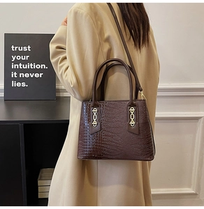Detail view of dark brown croc-effect tote bag with gold chain accents worn with beige coat