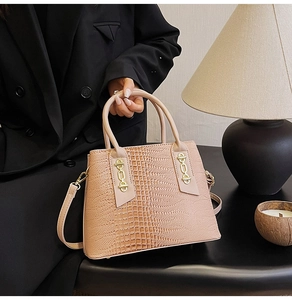 Detail of crocodile embossed pink handbag with gold hardware held by a fashion model