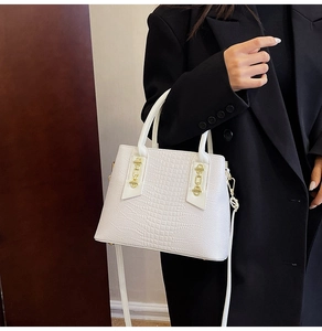 Detail of white crocodile pattern handbag with gold hardware chain on black blazer