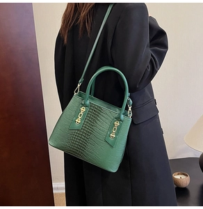 Detail of green crocodile texture handbag with gold hardware worn with black blazer