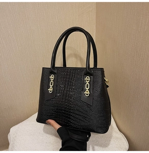 Detail of black crocodile texture handbag with golden chain accents and sturdy handles