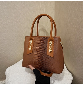 Detail of brown crocodile embossed tote bag with gold chain accents and leather texture