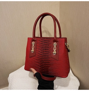 Detail view of red crocodile texture handbag with golden chain buckles and sturdy handle