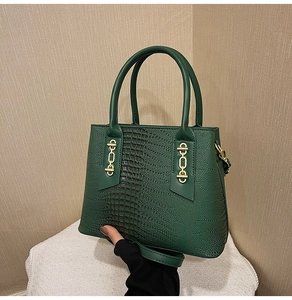 Detail of dark green tote bag with crocodile texture and gold H-shaped metal ornament