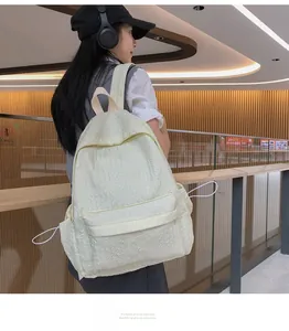 Détail d'un grand sac à dos beige avec texture gaufrée porté par un mannequin dans un hall