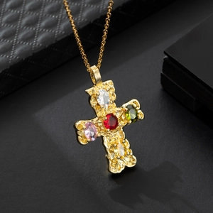 Collana a croce dorata con pietre preziose colorate su sfondo materico nero chic