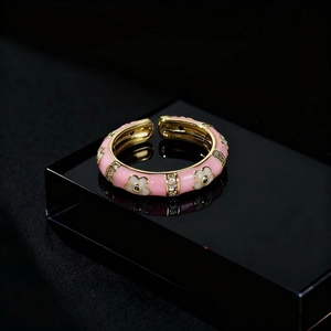 Pink enamel flower ring with sparkling zircons and a gold-tone band on a reflective base
