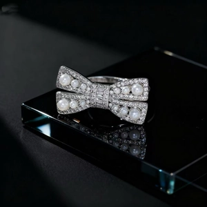 Elegant bow-shaped ring with pearls and pavé diamonds on a sleek black surface