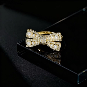 Elegant gold bow ring with white pearls and sparkling zircons on reflective surface