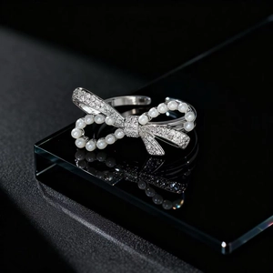 Macro detail of silver bow ring with white pearls and sparkling zircons on black surface