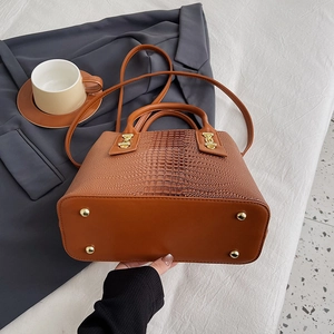 Brown crocodile embossed tote bag with top handle and gold studs shown in office setting