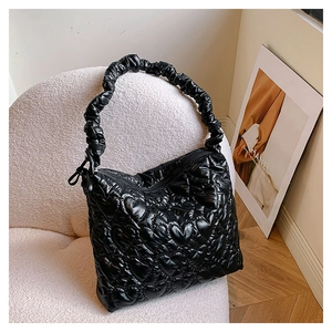 Detail of black quilted shoulder bag with heart pattern and ruched handle on a sofa
