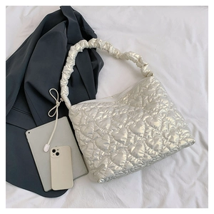 Detail showing silver heart-quilted shoulder bag with ruched handle on fabric background