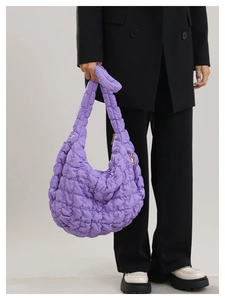 Detail view of purple quilted cloud shoulder bag in glossy nylon fabric carried by model