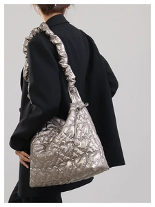 Detail of silver heart-quilted shoulder bag with ruffled strap worn on black blazer