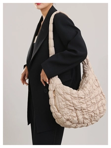 Detail showing the side gold zipper pocket of a large beige quilted cloud crossbody bag