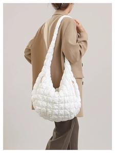 Close-up of white quilted puffer cloud bag with golden zipper on a beige blazer model