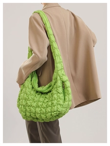 Close-up of bright green quilted cloud bag with puffy texture and wide shoulder strap