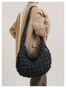 Detail of black quilted cloud bag showing shiny nylon fabric and gold zipper on model