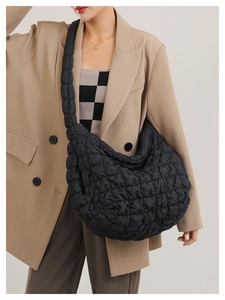 Side view of black quilted cloud bag with padded straps on a model in a beige blazer