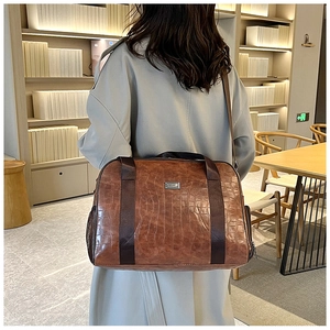 Dettaglio borsa da viaggio marrone in pelle PU con texture coccodrillo e logo in metallo