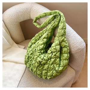 Detail of green quilted cloud bag on white textured sofa showing the soft nylon bubble texture