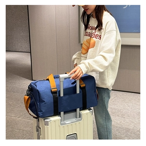 Bolsa de viaje azul con correas naranjas montada sobre el asa de una maleta