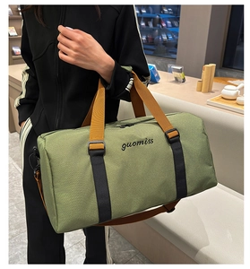 Detalle de bolsa de viaje en lona verde oliva con correas marrones y bordado fino
