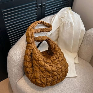 Quilted cloud puffer shoulder bag in caramel brown displayed on a modern fleece sofa