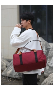 Red Oxford travel bag with brown leather handles worn by a model in outdoor setting