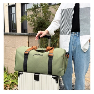 Green canvas travel tote with orange handles resting on white striped luggage case