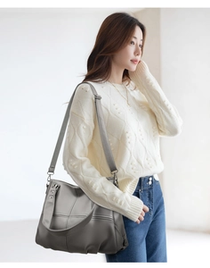Detailansicht einer dunkelgrauen Leder-Tote-Bag an einem Model mit weißem Pullover