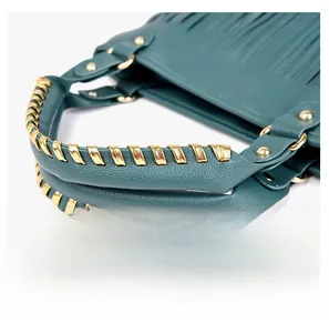 Dettaglio borsa in pelle verde scuro con manici intrecciati in metallo dorato e nappe