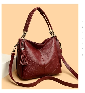 Detail of burgundy textured leather bag with V-shaped stitching and tassel accent