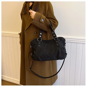 Detail of matte black tote bag with silver rivets and long strap on a brown coat
