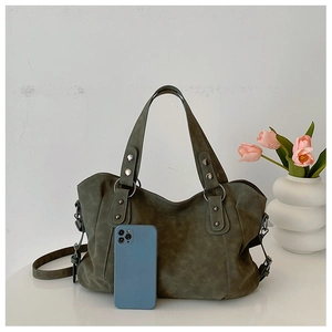 Detail of dark green suede tote bag with metal rivets and phone for size reference