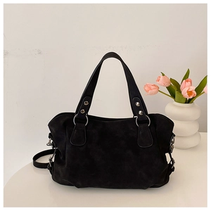 Detail of a vintage black matte leather tote bag with metal rivets on a white table