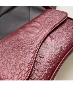 Détail de la texture cuir de crocodile bordeaux avec surpiqûres précises du sac