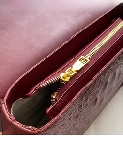 Détail de la fermeture éclair dorée et du cuir gaufré crocodile sur un sac bordeaux