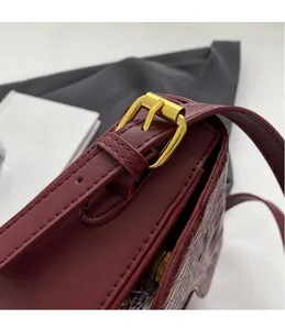 Vue macro de la boucle dorée et du cuir bordeaux texturé du sac à bandoulière