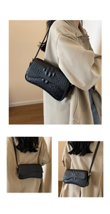 Détail de la texture crocodile noire et boucle en métal doré sur le sac à bandoulière